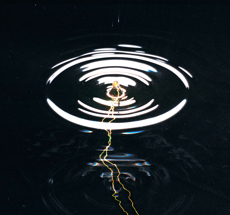 a photo of a drip of water hitting a body of water with lighting come out below it